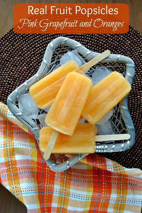 Overhead view of orange popsicles laying on ice in a silver metal basket with a colorful cloth napkin.