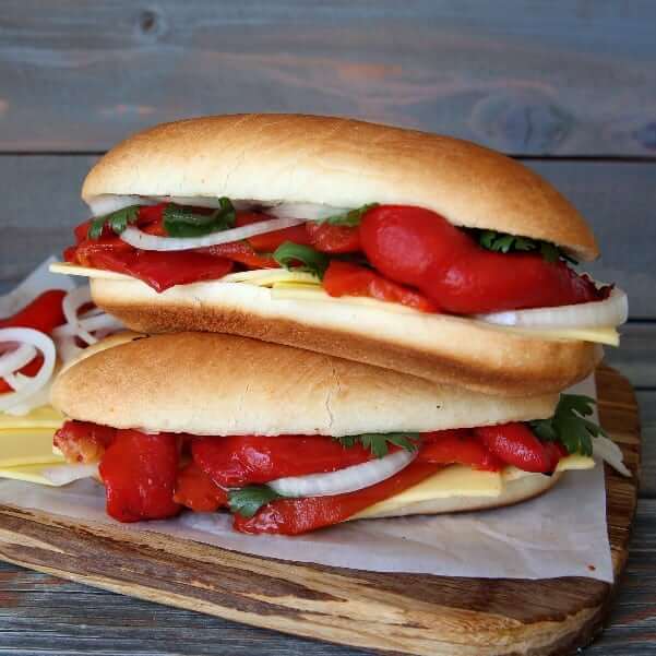 Front view photo of double stack stuffed baguette sandwiches on a wooden cutting board.