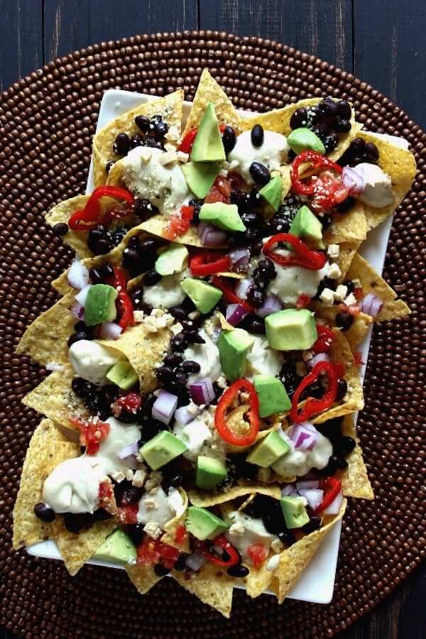 Overhead photo of nacho chips covered with fresh vegetables and vegan cheese. First photo for 27 Vegan Mexican Style Recipes.