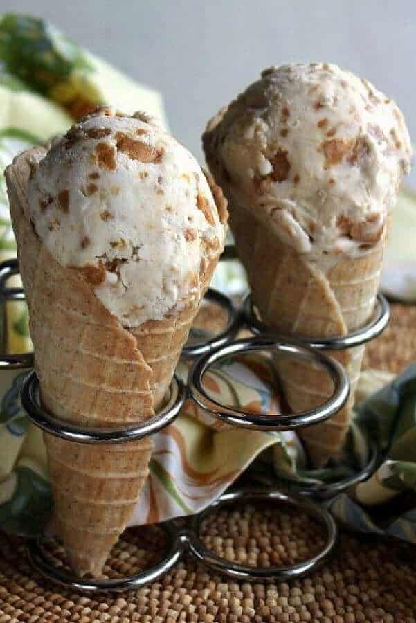 Two cones are full of ice cream sitting in a stainless ice cream cone holder.