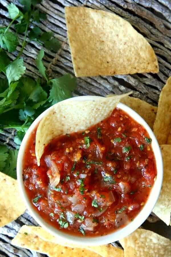 Overhead photo of a tortilla chip in Chunky Tomato Salsa in a white bowl and more chips.