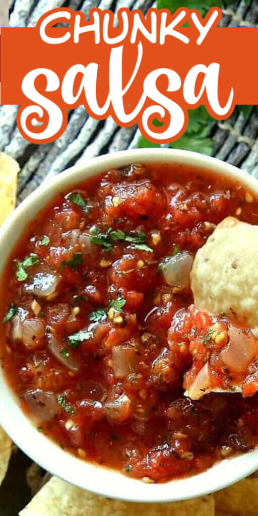 Overhead closeup view of chunky salsa in a white bowl and a chip scooping up a bite.