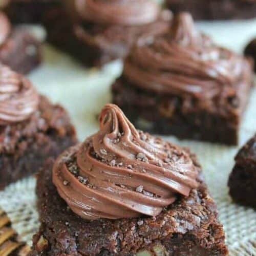Brownies are topped with a twirl of frosting and spread out at a tilted angle.