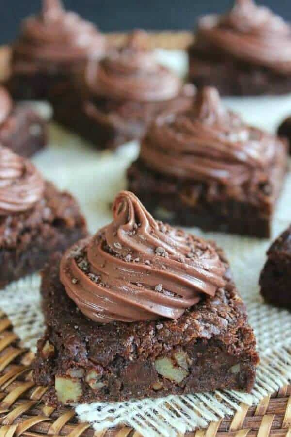 Vegan Chocolate Brownies are topped with a twirl of frosting and spread out at a tilted angle.
