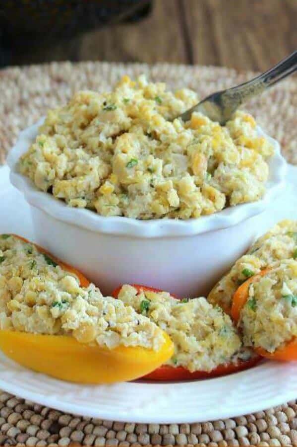 stuffed mini peppers on a plate with a bowl of stuffing behind.