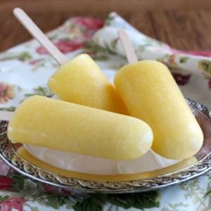 Three pineapple coconut popsicles laying on their side on a silver tray of ice.