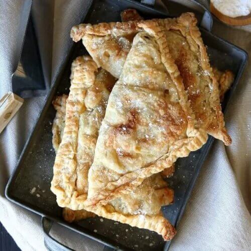 A square tin pan is filled with golden brown vegan apple turnovers.