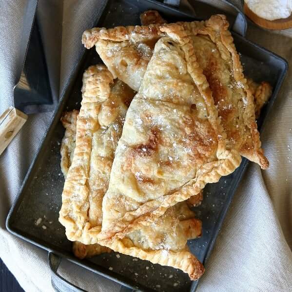 A square tin pan is filled with golden brown vegan apple turnovers.