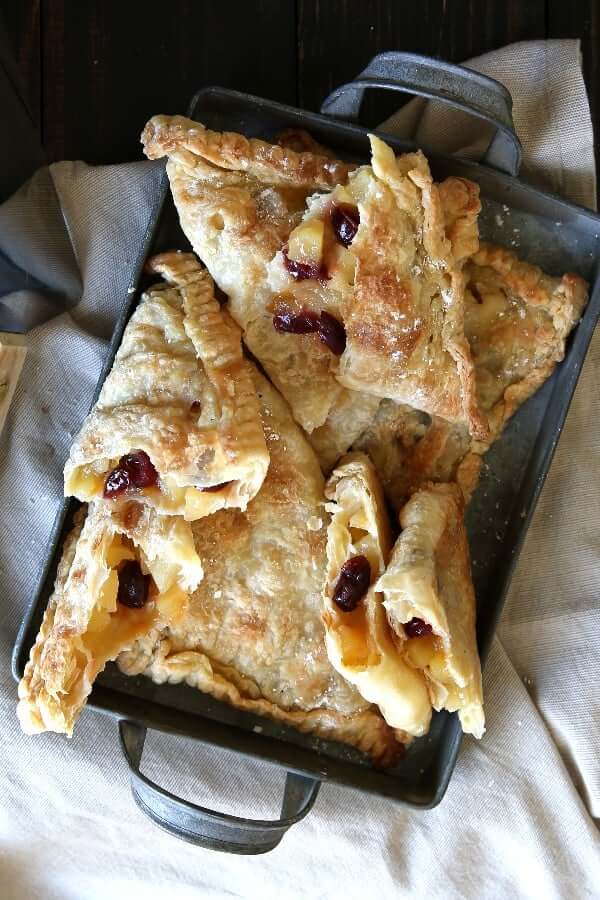 Ovehead photo of a pile of turnovers with three broken open to see the apples and cranberries baked in sweet fruity syrup.