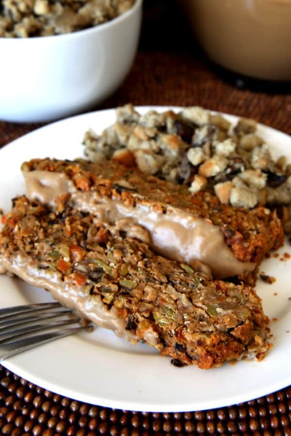 Two slices of Vegan Meatloaf with gravy and mushroom stuffing on a white plate.