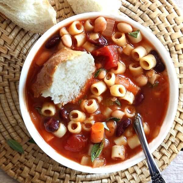 White bowls in an overhead photo filled with Pasta e Fagioli soup with bread dunking into the soup.