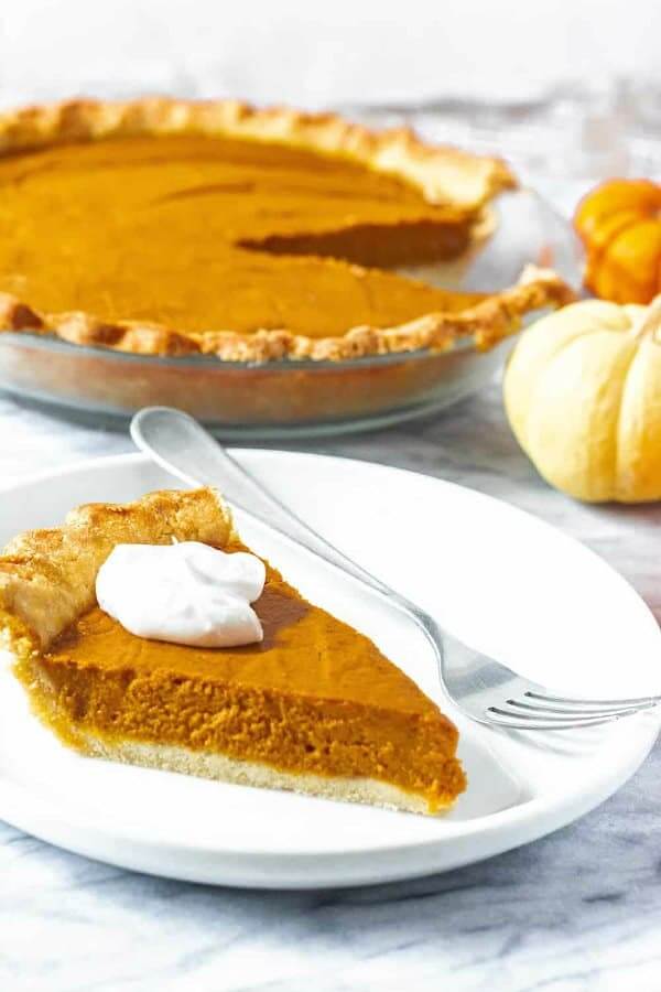 One slice of pumpkin pie in front of the whole pie.