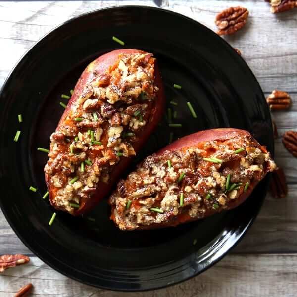 Two stuffed sweet potatoes vegan style dressed and on a black plate.