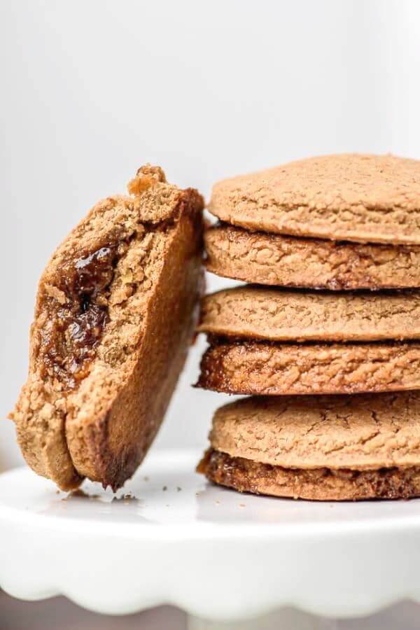 Stack of cookies with one leaning against them with a bite taken out to show the jam filling.