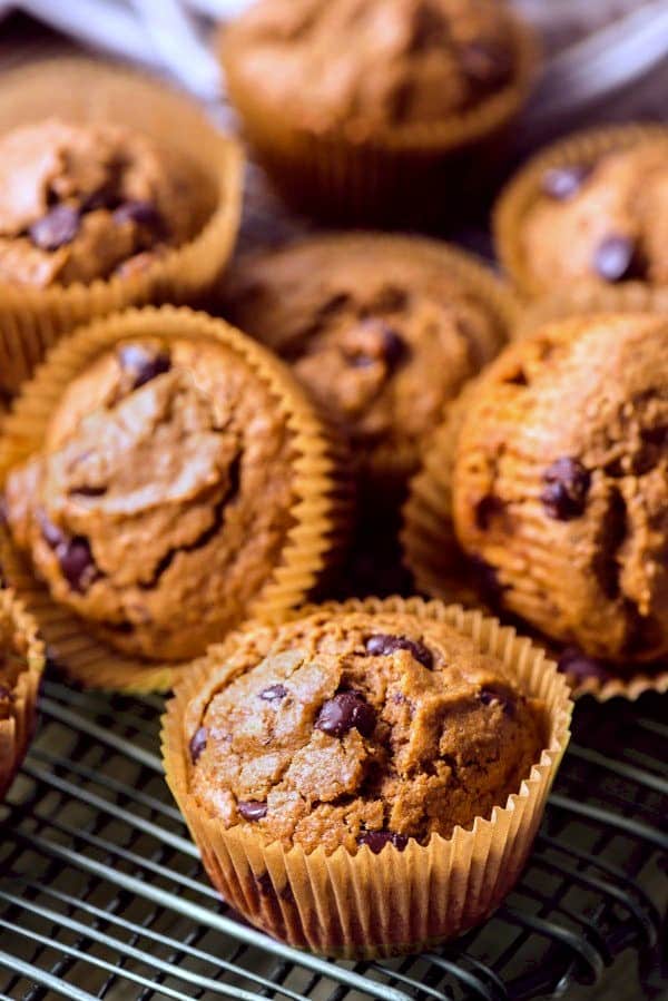 Lots of muffins are scattered in their cups on a cooling rack.
