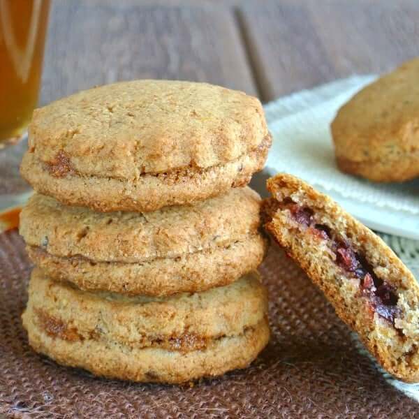 Scalloped edged jam filled cookies with one leaning on a stack of three.