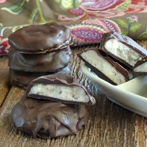 Homemade peppermint patties stacked and broken on a wooden table and in a white bowl.