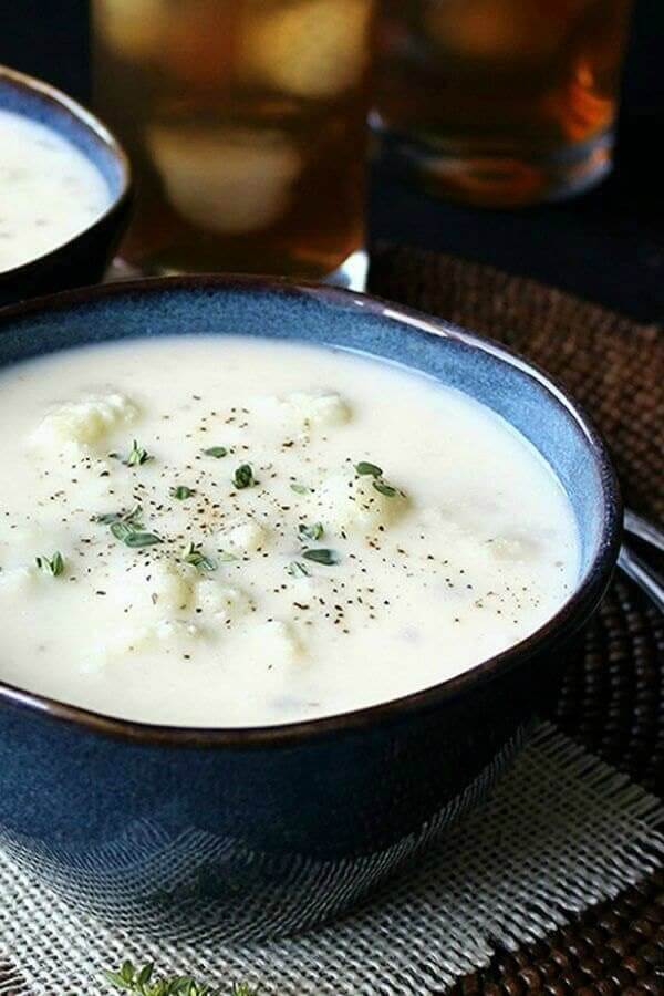 Creamy white cauliflower soup in a navy bowl on a woven mat.