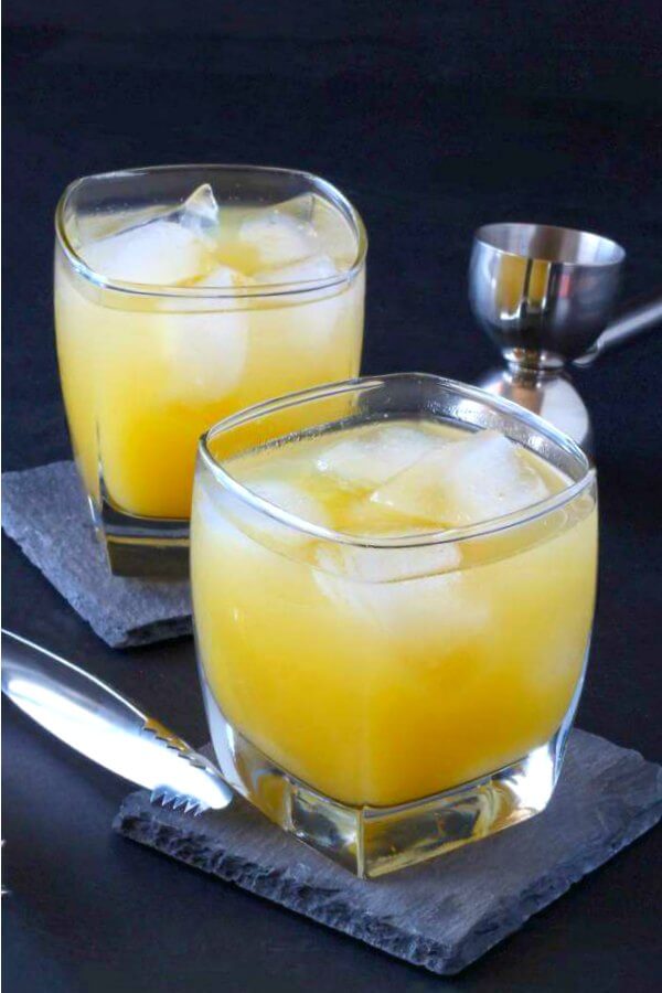 Two square cocktail glasses filled with a vodka and orange juice cocktail and ice cubes against a black background.