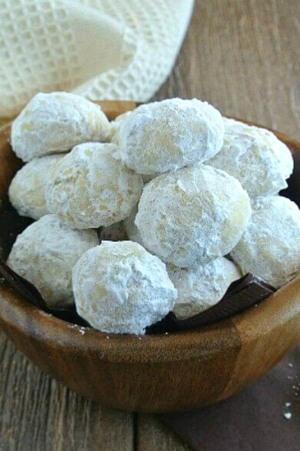 Wooden bowl full of cookie balls covered with powdered sugar.