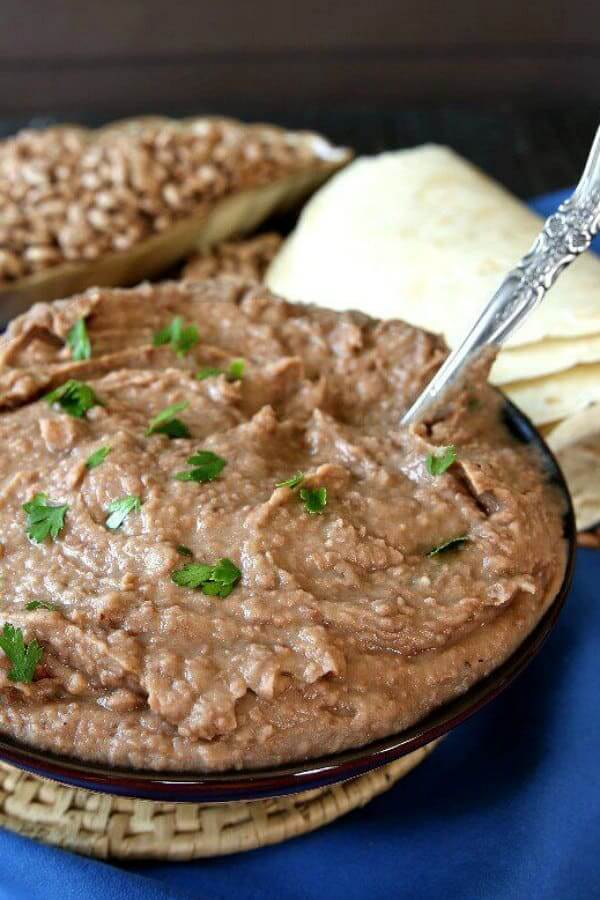 Close-up and tilted bowl full of homemade refried beans with tortillas on the side.