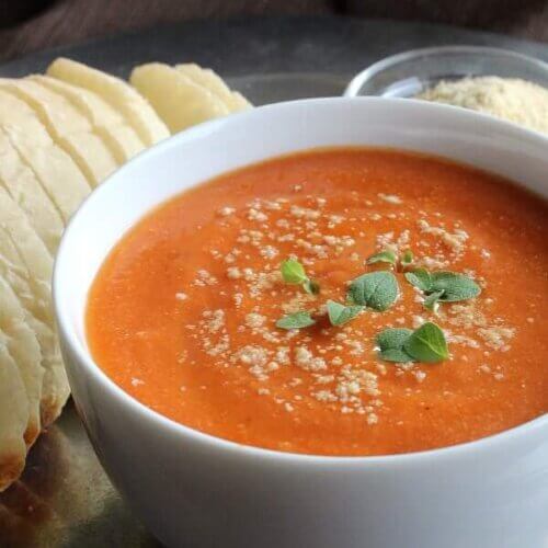 Cropped white bowl of dairy-free tomato soup with vegan parmesan cheese sprinkled on top.