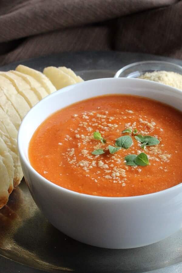 Cropped white bowl of dairy-free tomato soup with vegan parmesan cheese sprinkled on top.