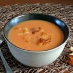 Beige bowl filled with crockpot tomato soup is tilted forward and sprinkled with croutons.