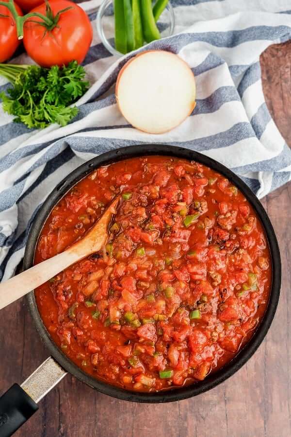 One skillet filled with a marinara sauce along with all of it's ingredients against a picnic table top.