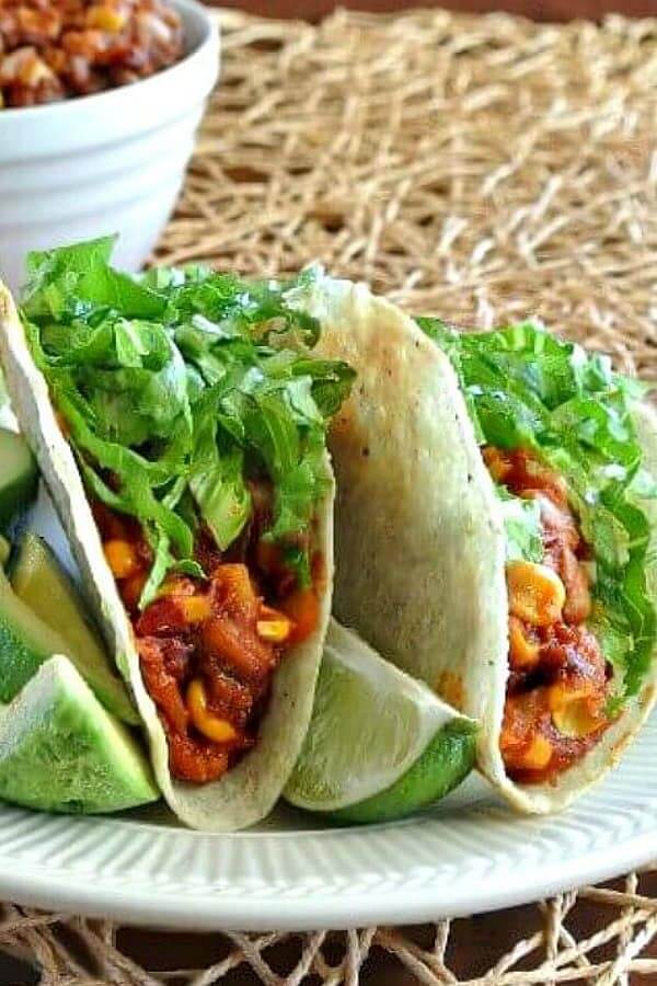 Two taco shells filled with a hot pinto beans and corn mixture with greens and avocado.