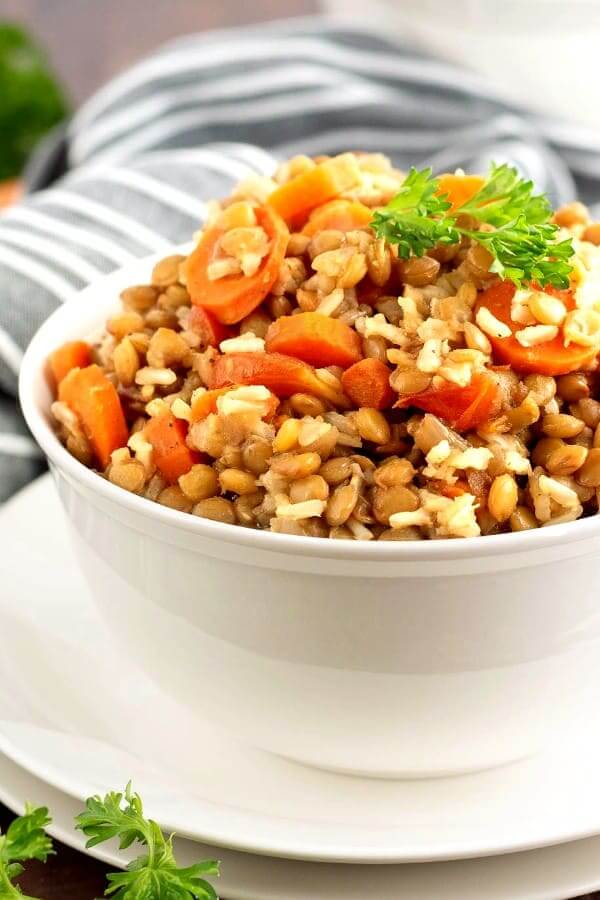 Side view of a white bowl piled with lentils, carrots and rice.