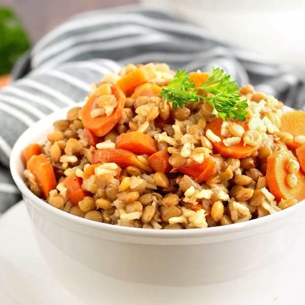 Close up cropped white bowl full of baked lentils and rice with carrots throughout.