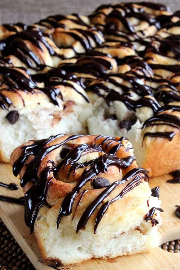 Close up of one chocolate drizzled cinnamon roll broken off the whole pan of rolls.