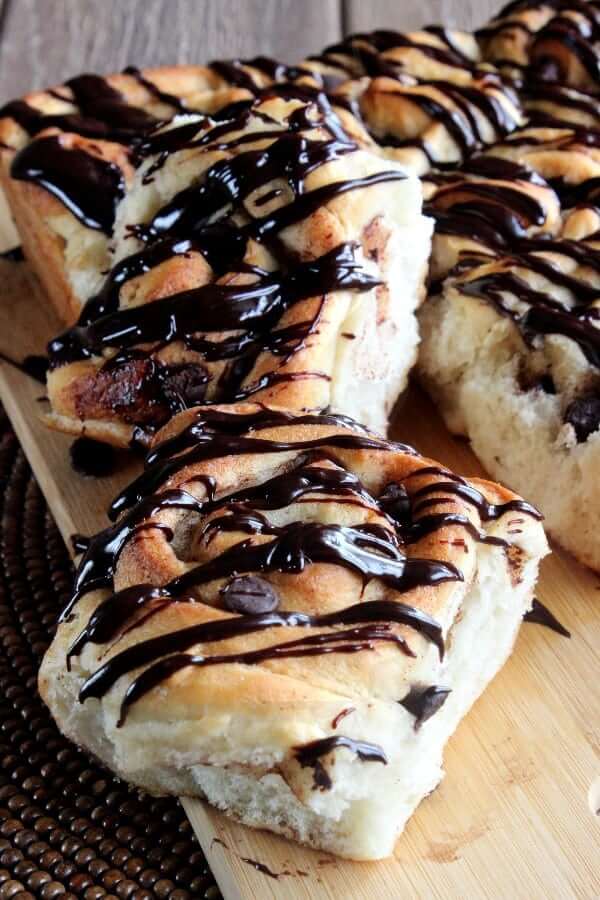 Close up of one chocolate drizzled cinnamon roll broken off the whole pan of rolls.