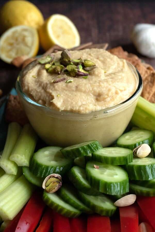 A bowl of white bean hummus with colorful veggies all around for dipping.