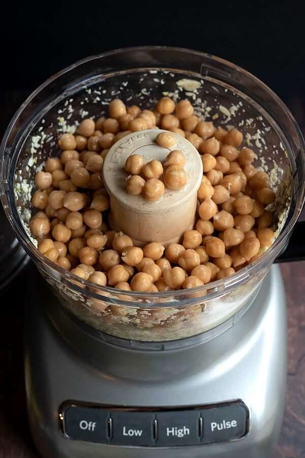 Ingredients along with chickpeas on top in a food processor before being processed.