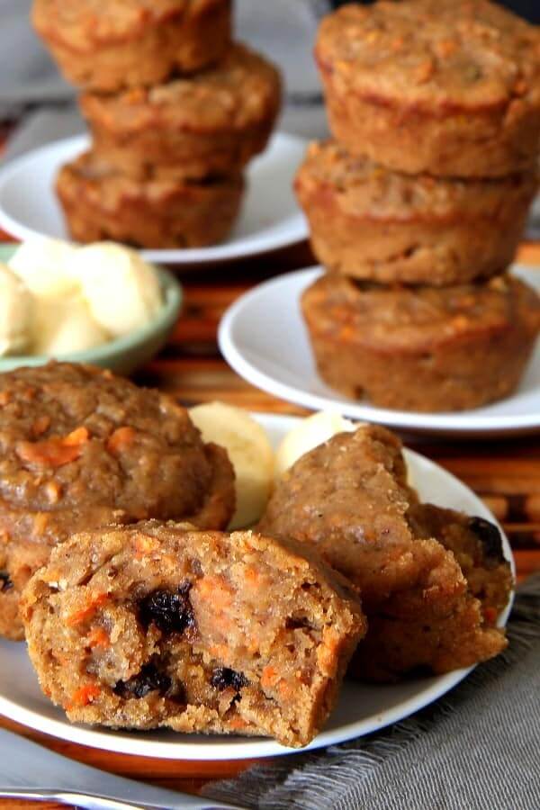 Close up of applesauce muffin opening on a plate with stacks of more muffins behind.