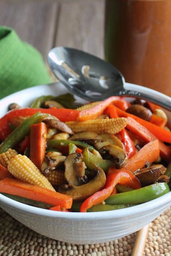 Titled view a lots of sauteed fresh veggies and baby corn with a slotted spoon on the side.