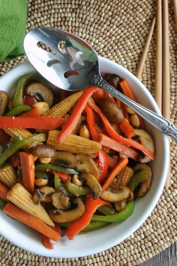 Overhead pic of a serving spoon leaning on a bowlful of colorful sliced and stir fried vegetables.