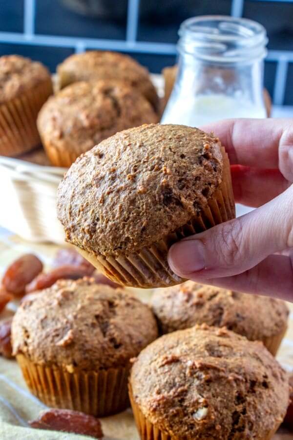 Holding a baked muffin in front of a bowlful of muffins with dates scarttered around.