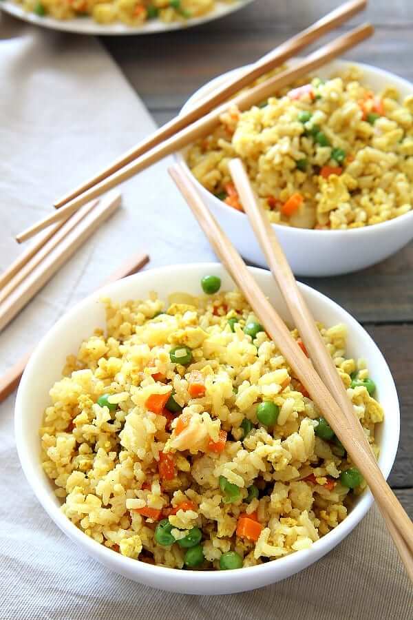 Two bowls full of tofu and veggies fried rice with chopsticks laying on the rims.
