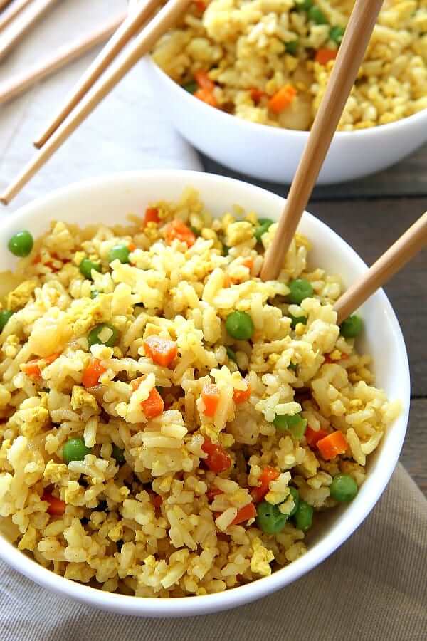 Close up photo of a tilted bowl with finished fried rice and chopsticks.