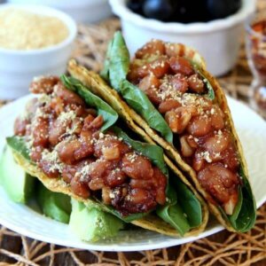 Square photo of two close up pinto beans tacos on a white plate and open straw mat.