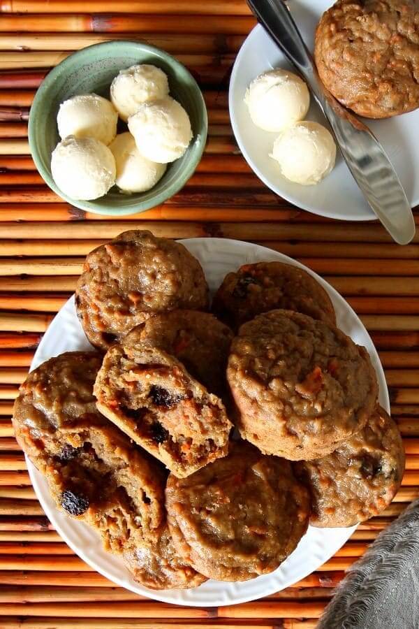 Overhead photo a a huge pile of healthy carrot muffins with dairy free butter and a spreading knife on the side.