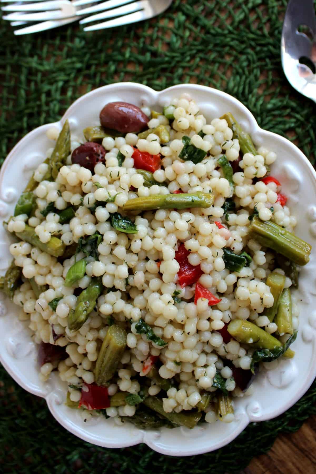 Looking down at a beautiful white bowl filled with cooked and fresh grains and vegetables against a forest green mat.