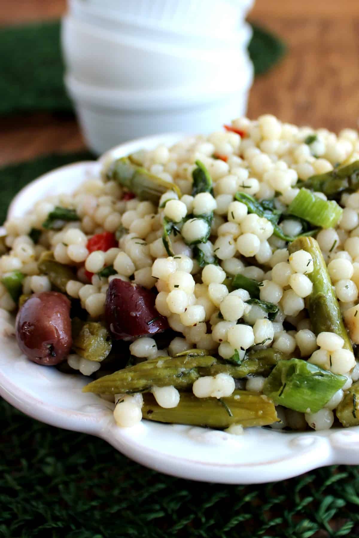 Tilted and photo cropped bowl full of pearl couscous and veggies. All against a forest green woven mat.