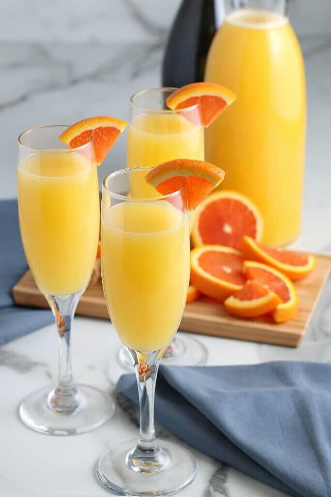 Styles photos with three champagne glass filled with mimosas and quarter slices of an orange.