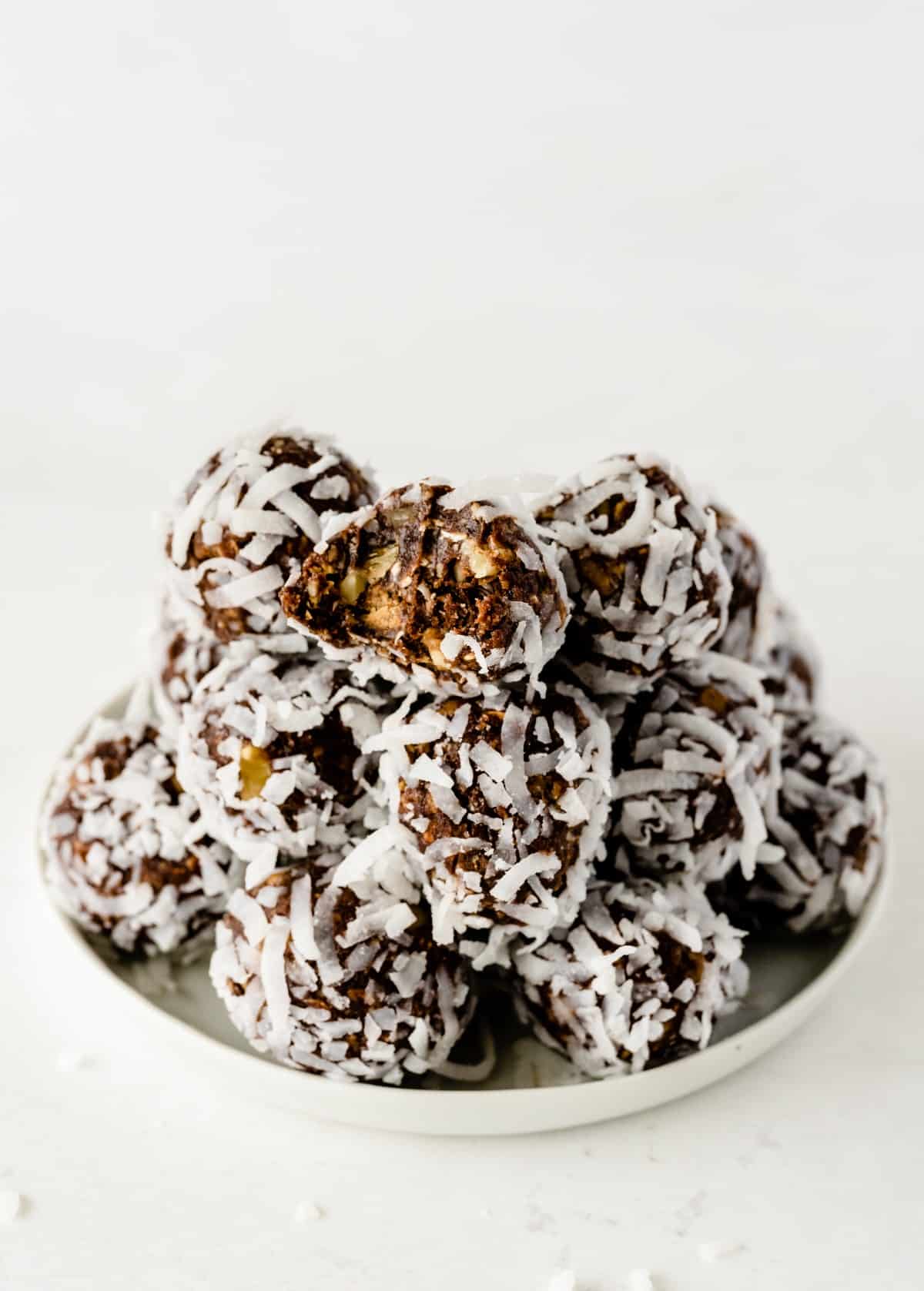 A white plate is piled high with chocolate date energy balls with the top one having a bite out of it.