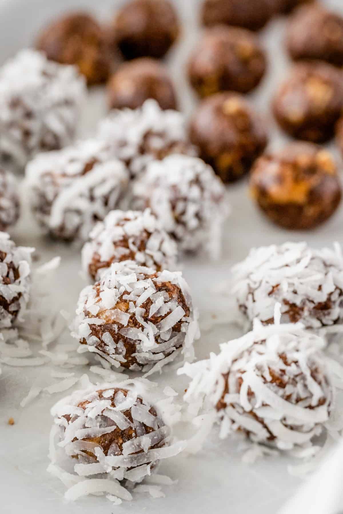 Close up of date energy balls loaded onto parchment paper where some are covered in coconut and some are not.