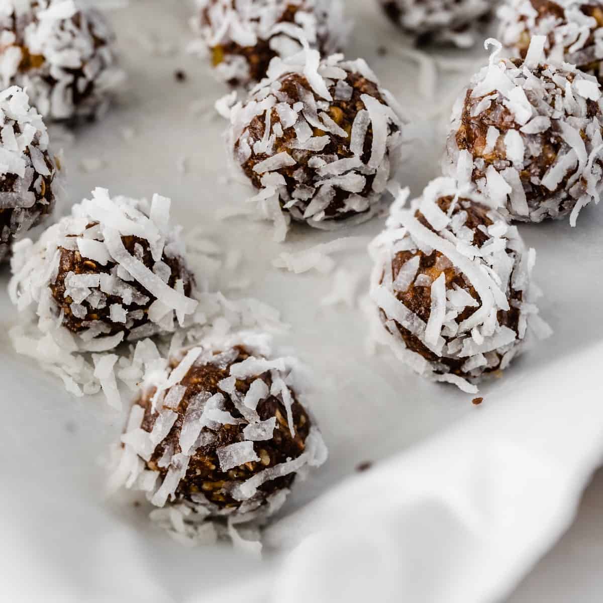 A close up of a few coconut covered chocolate date balls on a cookie sheet and parchment paper.